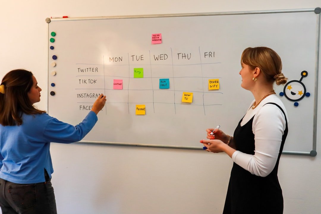 two women standing in front of a whiteboard with sticky notes on it